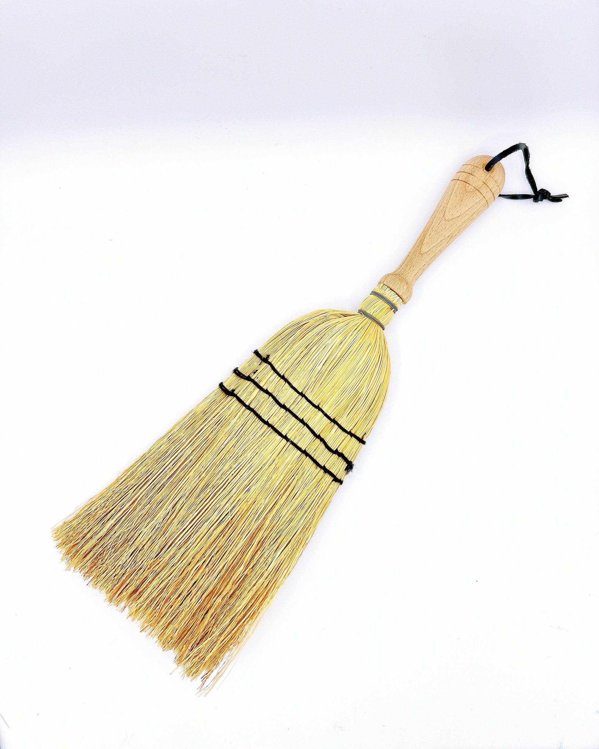 Redecker hand broom with rice straw bristles and a smooth wooden handle, designed for quick sweeping of small spaces.