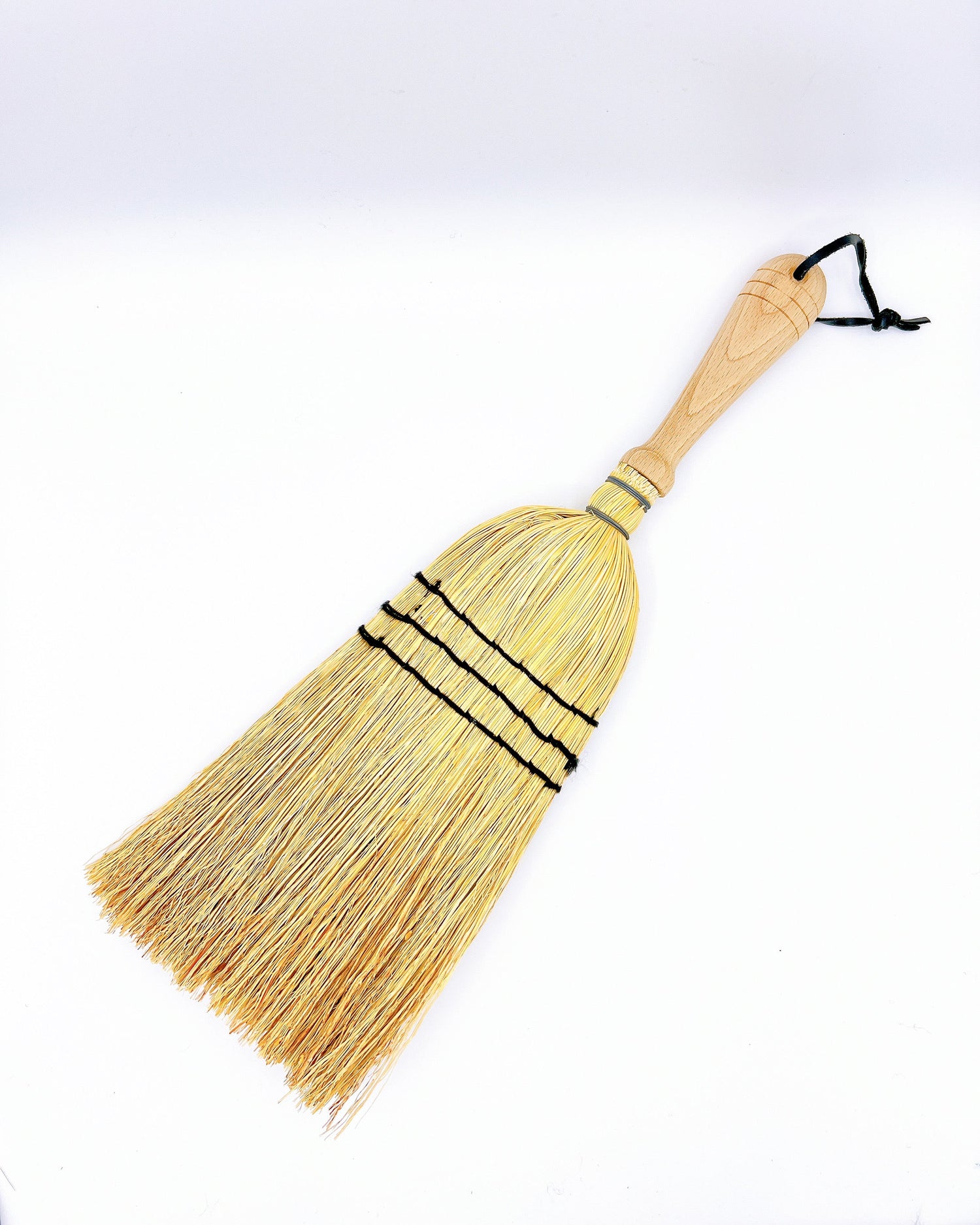 Redecker hand broom with rice straw bristles and a smooth wooden handle, designed for quick sweeping of small spaces.